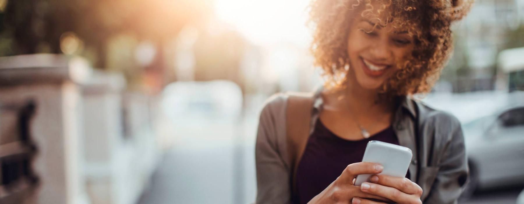 woman texts on her phone as she walks through the city