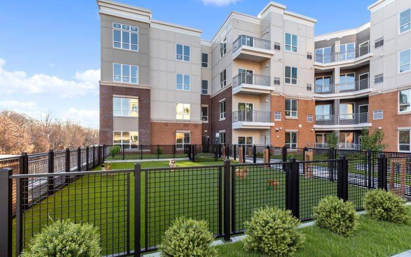 a fenced in dog park with buildings in the background